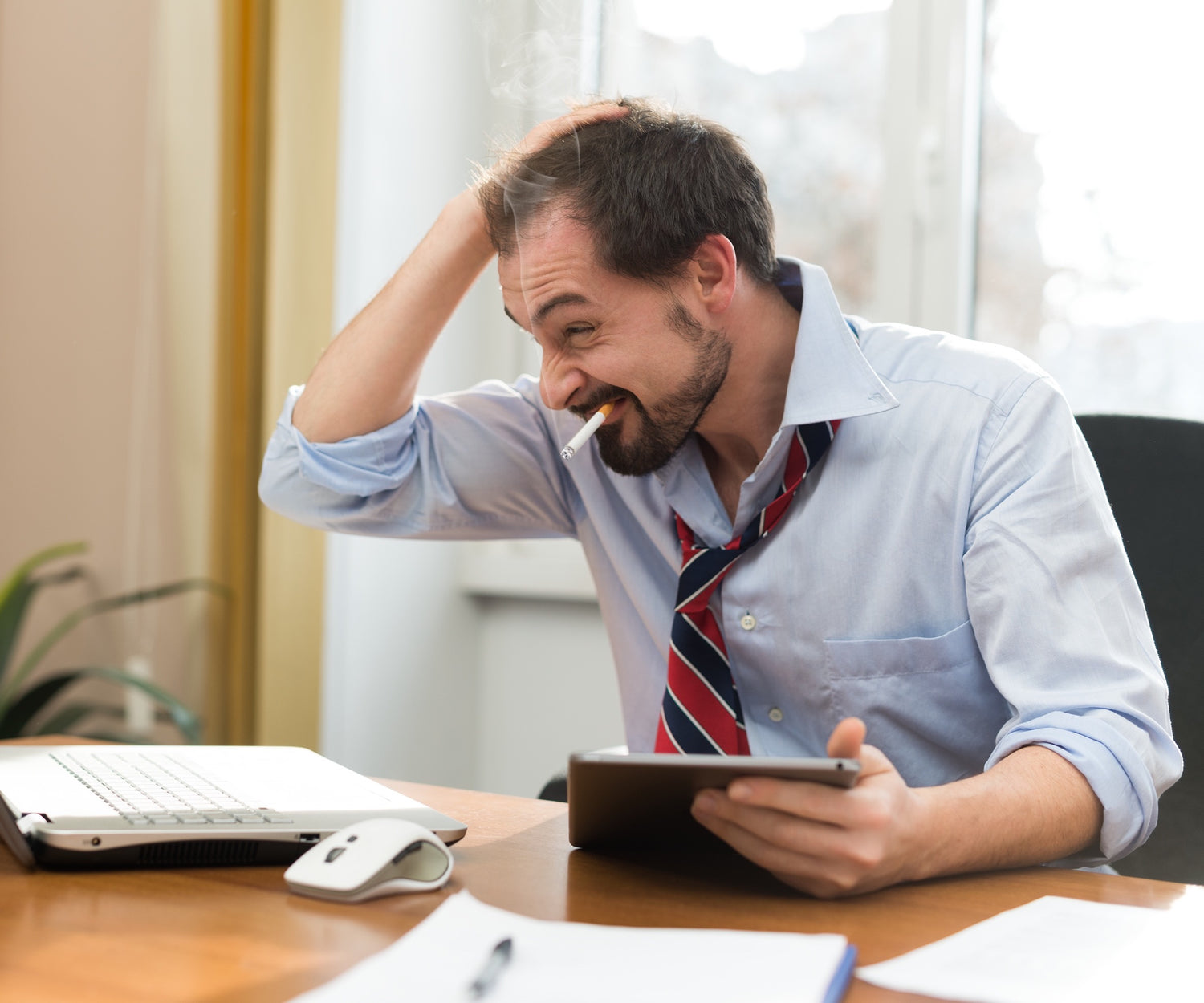 Image of a frustrated man smoking a cigarette while holding a tablet.